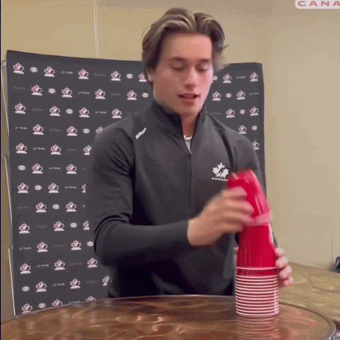 A Man In A Black Jacket With A Maple Leaf On It Stacks Red Cups GIF