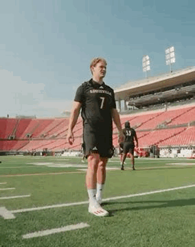 a man in a black jersey is standing on a football field .