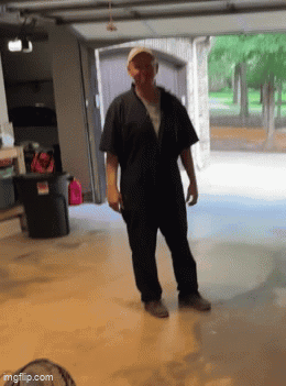 A Man In A Black Jumpsuit Is Standing In Front Of A Garage Door . GIF