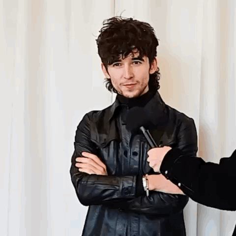 A Man In A Black Leather Jacket Is Being Interviewed By Someone With A Microphone GIF