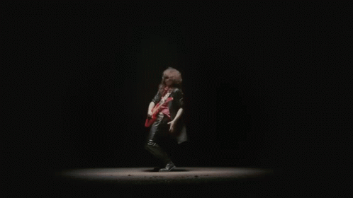 a man in a black leather jacket is playing a red electric guitar in the dark .