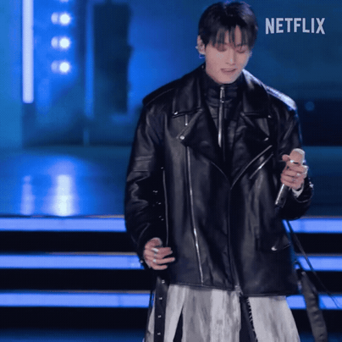 a man in a black leather jacket is singing into a microphone with netflix written on the bottom