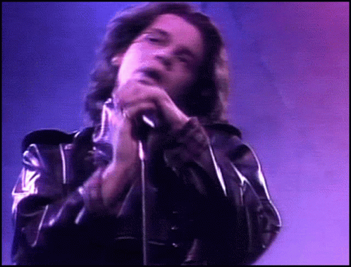 A Man In A Black Leather Jacket Singing Into A Microphone GIF