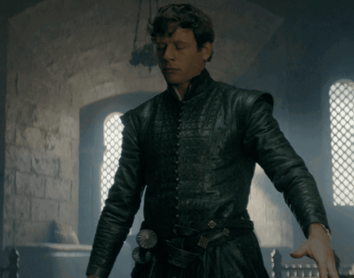 A Man In A Black Leather Jacket Stands In Front Of A Brick Wall GIF