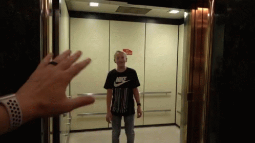 A Man In A Black Nike Shirt Is Standing In An Elevator GIF