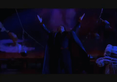 A Man In A Black Robe Is Standing In A Dark Room With His Arms Outstretched In Front Of A Group Of Bats . GIF