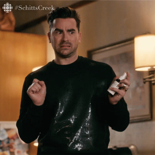 A Man In A Black Sequined Shirt Is Holding A Small White Bottle Of Something GIF