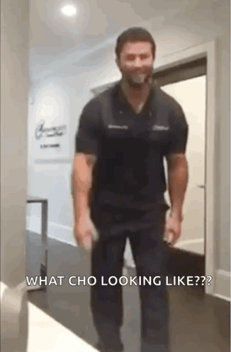 A Man In A Black Shirt And Black Pants Is Walking Down A Hallway With A Bottle In His Hand . GIF