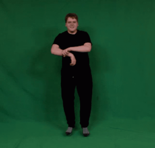 A Man In A Black Shirt And Black Pants Stands In Front Of A Green Screen GIF
