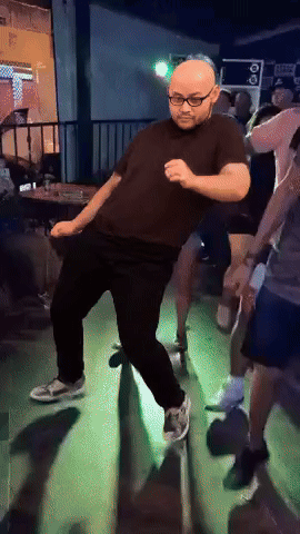 A Man In A Black Shirt And Glasses Is Dancing In A Dark Room GIF