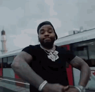 A Man In A Black Shirt And Hat Is Standing In Front Of A Bus . GIF