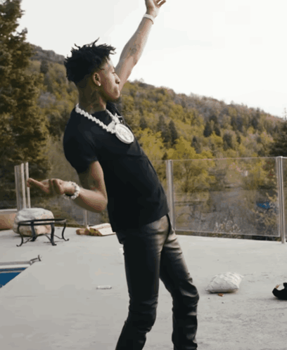 A Man In A Black Shirt And Leather Pants Stands On A Patio With His Arms In The Air GIF