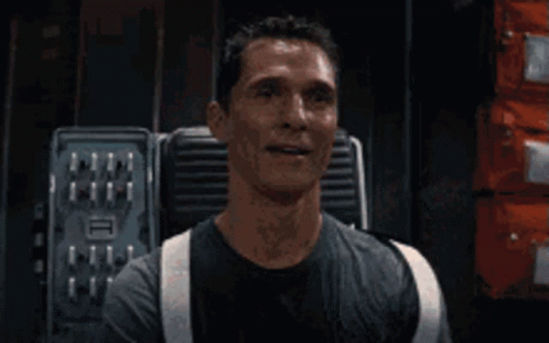 A Man In A Black Shirt And Suspenders Is Smiling In A Room . GIF