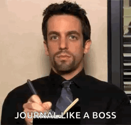 A Man In A Black Shirt And Tie Is Holding A Pen And Writing In A Notebook . GIF
