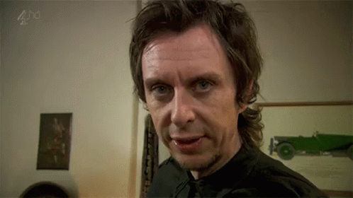 A Man In A Black Shirt And Tie Is Making A Funny Face In A Room . GIF