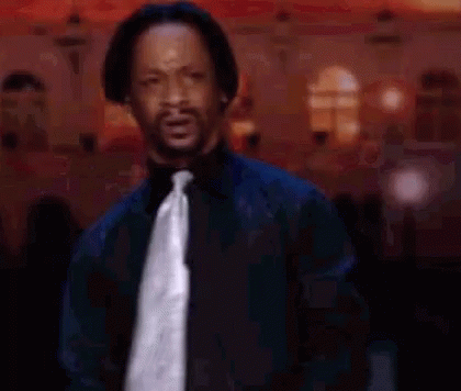 A Man In A Black Shirt And Tie Is Standing In Front Of A Crowd And Making A Funny Face . GIF