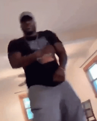 A Man In A Black Shirt And White Pants Is Standing In A Living Room . GIF