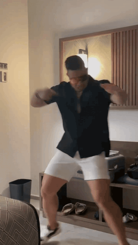 A Man In A Black Shirt And White Shorts Is Dancing In A Bedroom GIF