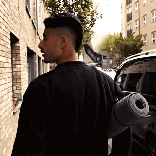 a man in a black shirt carrying a yoga mat on his back