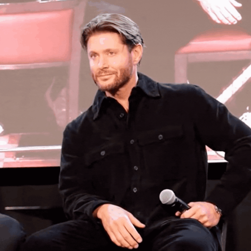 A Man In A Black Shirt Holds A Microphone In His Hand GIF