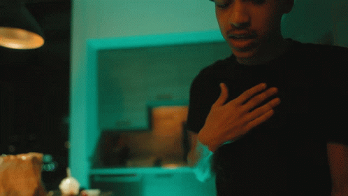 A Man In A Black Shirt Holds His Hand To His Heart GIF