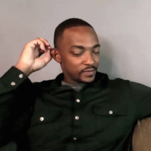 A Man In A Black Shirt Is Adjusting His Ear While Sitting On A Couch . GIF