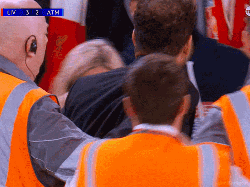 A Man In A Black Shirt Is Being Helped By A Man In An Orange Vest During A Liv 3 2 Atm Soccer Game GIF