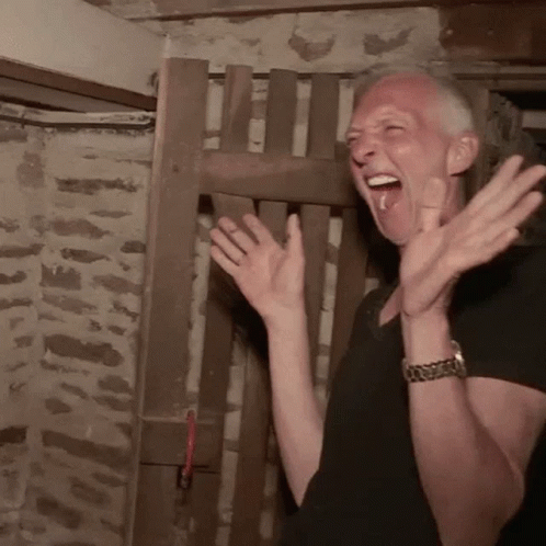 A Man In A Black Shirt Is Clapping His Hands In Front Of A Wooden Fence GIF