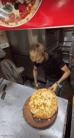 A Man In A Black Shirt Is Cutting A Pizza On A Table GIF