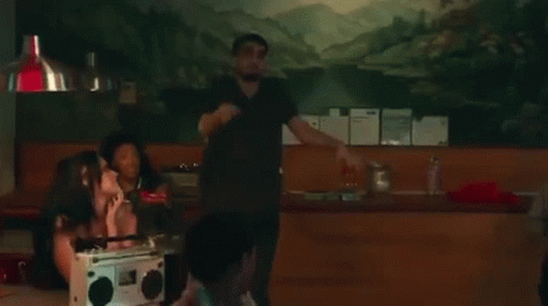 A Man In A Black Shirt Is Dancing In A Room With A Group Of People . GIF