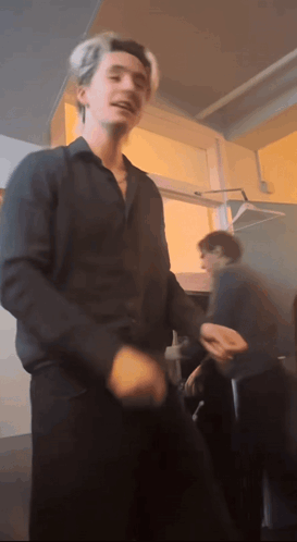 A Man In A Black Shirt Is Dancing In A Room With Other People GIF