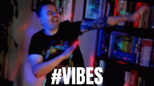 A Man In A Black Shirt Is Dancing In Front Of A Bookshelf With The Words #Vibes Above Him GIF