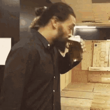 A Man In A Black Shirt Is Drinking A Glass Of Beer . GIF
