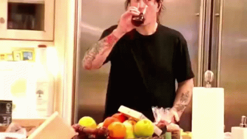 A Man In A Black Shirt Is Drinking A Glass Of Soda In A Kitchen . GIF