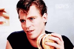 A Man In A Black Shirt Is Eating A Burger GIF