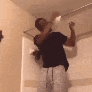 A Man In A Black Shirt Is Hanging Upside Down From A Ceiling . GIF