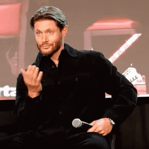 A Man In A Black Shirt Is Holding A Microphone And Making A Face GIF