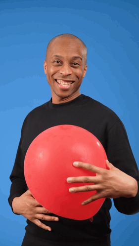A Man In A Black Shirt Is Holding A Red Balloon In His Hand GIF