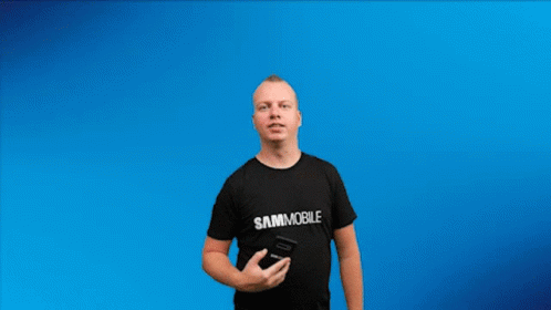 A Man In A Black Shirt Is Holding Up An Android 10 Phone GIF
