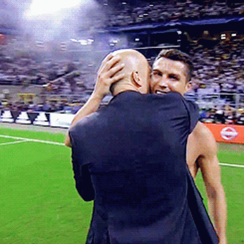 A Man In A Black Shirt Is Hugging Another Man On A Field GIF