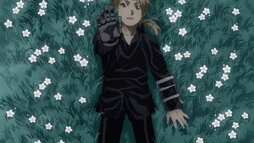 A Man In A Black Shirt Is Laying In A Field Of Flowers GIF