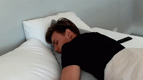 A Man In A Black Shirt Is Laying On A Bed GIF
