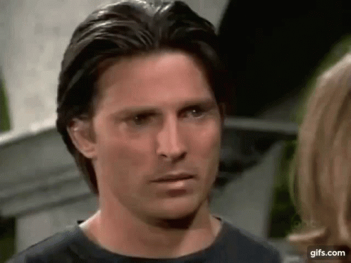 A Man In A Black Shirt Is Looking At A Woman In A Kitchen . GIF