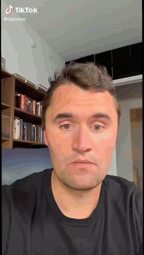 a man in a black shirt is looking at the camera with a bookshelf in the background