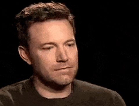A Man In A Black Shirt Is Making A Funny Face In A Dark Room . GIF