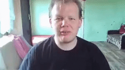 A Man In A Black Shirt Is Making A Funny Face While Sitting In A Living Room . GIF