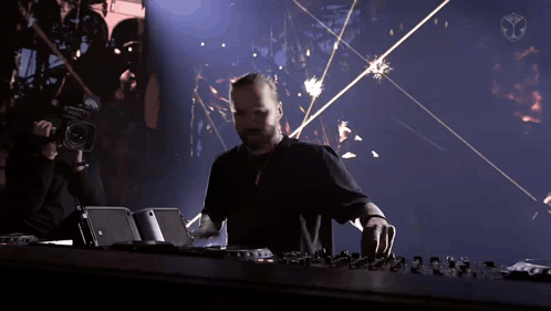 A Man In A Black Shirt Is Playing A Dj Set With A Camera Behind Him GIF