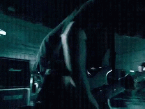 A Man In A Black Shirt Is Playing A Guitar In A Dark Room GIF