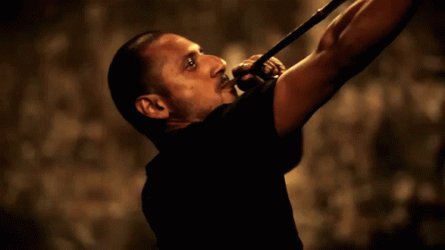 A Man In A Black Shirt Is Playing A Trumpet In A Dark Room GIF