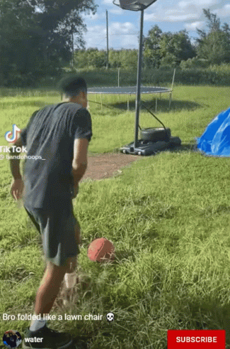 A Man In A Black Shirt Is Playing Basketball In A Field With A Trampoline In The Background GIF